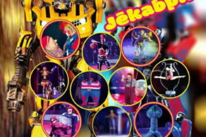 Cirka reklāmas plakāts, kurā dominē liels dzeltens Transformeru robots, ar tekstu "CIRKA IZRĀDE AR TRANSFORMERI Jēkabpils". Ap robotu ir aplīši ar attēliem, kas attēlo dažādus cirka numurus: klaunus, akrobātus, citus robotus un basketbola trikus. Apakšā uz rozā fona ir informācija: "1. marts. plkst. 12.00 Vecpilsētas laukums 3, Jēkabpils Tautas nams. Biļetes var iegādāties bilesuparadize.lv Tālr. uzziņām: 29860454.