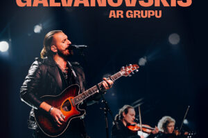 Miks Galvanovskis melnā ādas jakā dzied mikrofonā un spēlē akustisko ģitāru, ko apgaismo prožektori. Fonā redzami vēl divi grupas dalībnieki, kas spēlē vijoles. Attēlā ir teksts: "1. martā plkst. 15.00 Viesītes kultūras centrs SĒLIJA Koncerts MIKSS GALVANOVSKIS AR GRUPU Biļetes: Biļešu Paradīze un Viesītes KC".